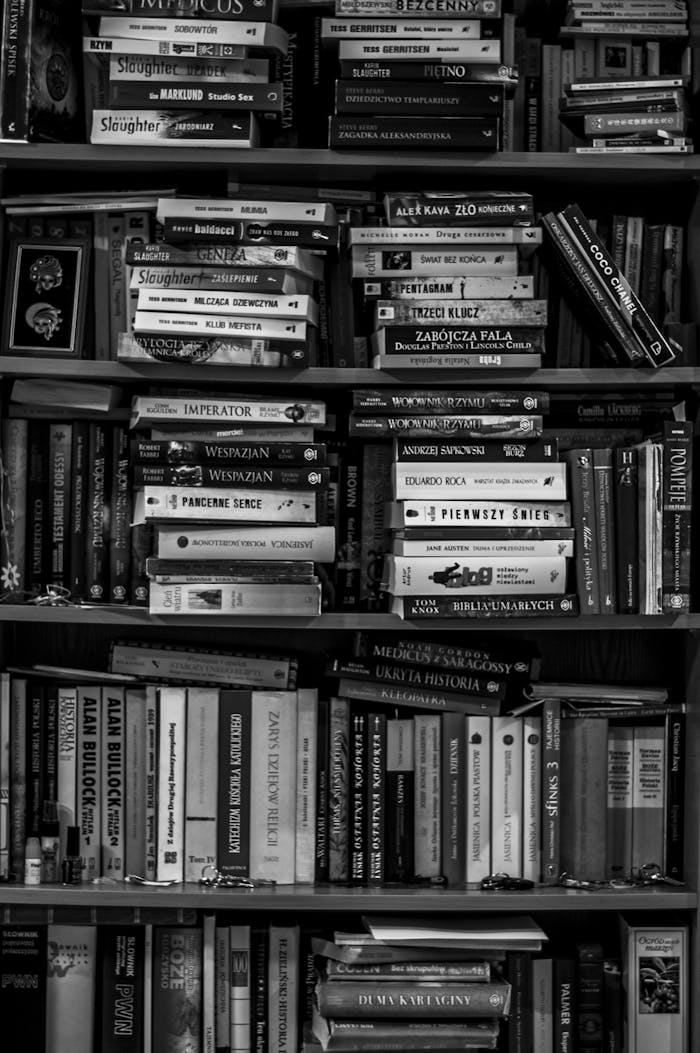 A black and white image of a packed bookshelf with various books in a library setting.